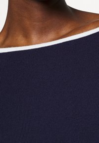 Detailní záběr na krk a rameno osoby, která má na sobě tmavě modrý žebrovaný top s bílým okrajem kolem výstřihu.