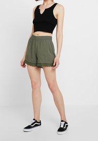 Černý žebrovaný krátký top s V- výstřihem; olivově zelené šortky s krajkovým lemováním; doplněné černo-bílými teniskami. Minimalistický design.