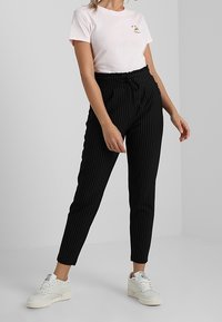 Pantalon noir à rayures avec une taille élastique, associé à un t-shirt rose clair avec un petit design graphique, et des baskets blanches.
