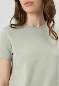 Lichtgroen T-shirt met korte mouwen en een ronde halslijn. Glad stof met een subtiele textuur, zonder zichtbare patronen of versieringen.