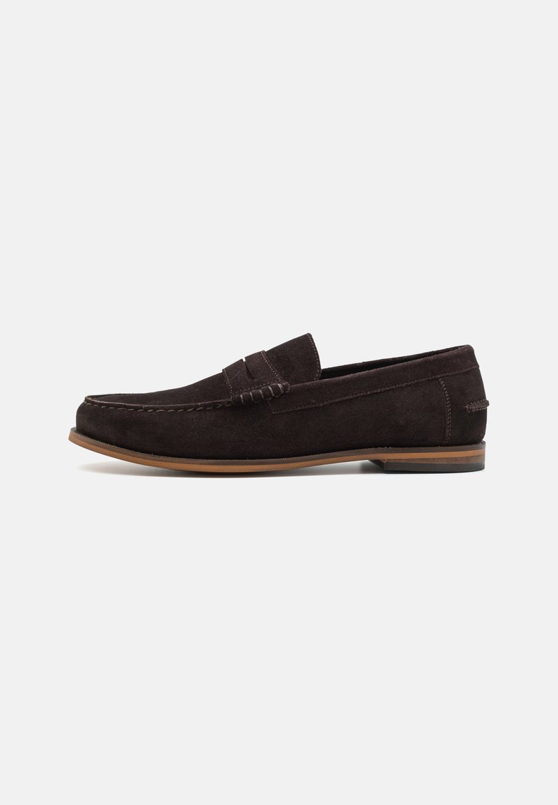 Mocassins en daim marron foncé avec un bout arrondi, une tige texturée et une semelle en caoutchouc marron clair. Présente une sangle décorative sur le devant.