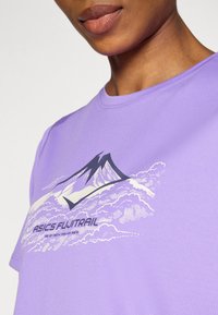 Μωβ κοντομάνικο μπλουζάκι με γραφικό βουνού και σύννεφα, με το κείμενο «ASICS FUJITRAIL» σε αντίθετο χρώμα. Μαλακή υφή υφάσματος.