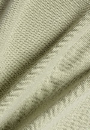 Lysebeige strikket stof med glat, fin tekstur vist i nærbillede med bløde folder, der skaber blide skygger.