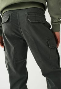 Dunkelgraue Cargo-Hosen mit glatter Textur, die zwei Gesäßtaschen und verstärkte Nähte haben. Das Design umfasst eine lockere Passform und Seitentaschen.