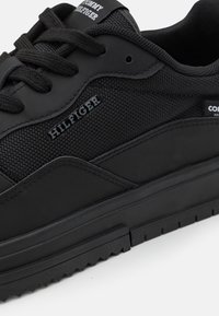 Baskets noires avec une tige en mesh texturé et des accents synthétiques lisses, lacets noirs et semelle en caoutchouc à crampons. Logo de la marque affiché.