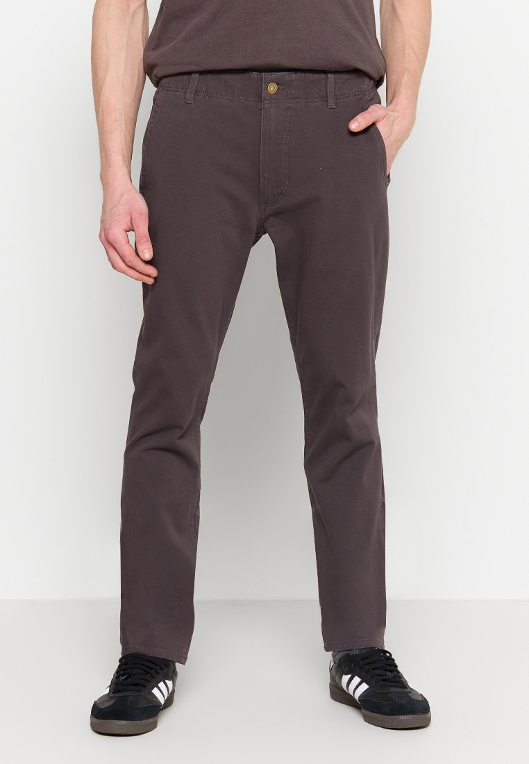 Pantalon gris foncé pour homme, coupe slim, en matière mélangée coton, avec poches avant et un bouton doré. Stylé avec des chaussures de sport noires.
