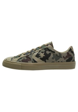 Zapatilla baja con patrón de camuflaje verde y marrón, suela de goma beige y cordones a juego, vista de perfil.