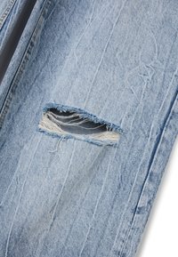 Jeans de mezclilla azul claro con un diseño desgastado que presenta un gran corte que expone bordes deshilachados y mezclilla oscura por debajo.