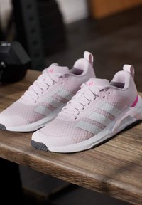 Hellrosa Sportschuhe mit weißen Streifen, Mesh-Material und strukturierter Oberfläche. Ausgestattet mit einer Zuglasche und einer grauen Gummisohle.