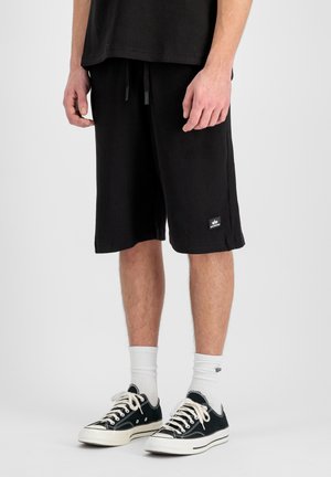 Man wearing black ribbed shorts, white crew socks, and black low-top sneakers with white laces, standing against a plain background.
