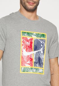 Grå T-shirt med farverigt grafisk tryk i røde, grønne og blå sektioner. Indeholder Nike-logo i hvid. Korte ærmer, rundt snit.