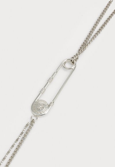 Colar prateado com um grande pingente em forma de alfinete de segurança, com um encanto circular gravado com um leão e um padrão de chave grega, corrente texturizada.