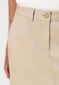 Beige Baumwollshorts mit Knopfverschluss, Gürtelschlaufen und Seitentaschen mit einer glatten Textur.