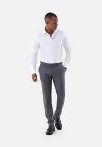 Weißes Hemd mit Knöpfen, maßgeschneiderte graue Hose und schwarze Leder Schuhe. Slim Fit und glatter Stoff mit einer dezenten Textur.