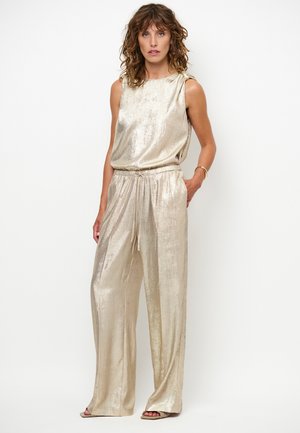 Gouden metallic jumpsuit met mouwloos topje, elastische tailleband en wijde pijpen. Glad oppervlak en lichte glans benadrukken het ontwerp.