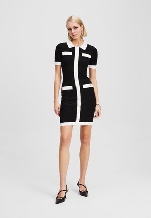 Black fitted dress with textured fabric, short sleeves, white collar and pockets, and vertical white stripe down the front.