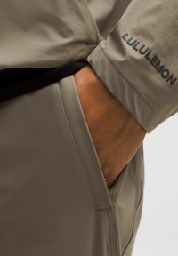 Lichtbeige broeken met een gladde, soepele textuur. Voorzien van een zwarte tailleband en een zichtbaar Lululemon-logo op de zoom.