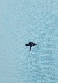 Lichtblauwe gebreide trui stof met een klein, donkerblauw geborduurd boomlogo aan de linkerkant. Vrouwelijke textuur, eenvoudig ontwerp.