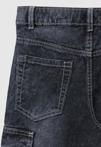 Tessuto di denim nero con una consistenza morbida, dotato di una tasca posteriore singola e cuciture bianche a contrasto. Design a vita alta.