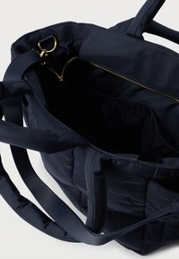 Granatowa pikowana torba typu tote z dwoma solidnymi uchwytami, zamykana na zamek błyskawiczny z złotym detalem. Miękka w dotyku, z przestronnym wnętrzem.