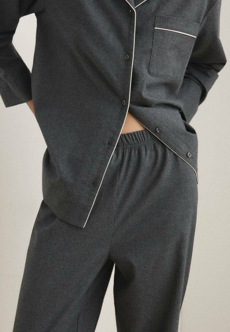 Conjunto de pijama de un gris oscuro con una camisa abotonada que presenta un bolsillo en el pecho y ribetes blancos, combinado con pantalones de cintura elástica. Textura de tela suave.