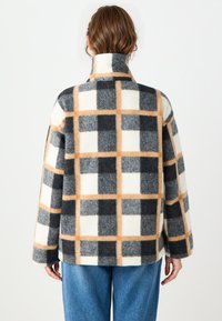 Geverifieerde wollen jas met een hoge kraag, voornamelijk zwart, wit en oranje ruitpatroon, en een ontspannen pasvorm met lange mouwen.