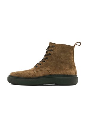 Bottines en daim marron avec des lacets noirs, bout arrondi, semelle en caoutchouc verte et une languette à l'arrière pour un enfilage facile.