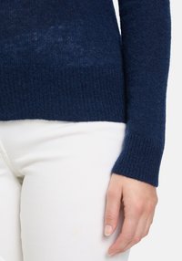 Pullover blu navy in maglia con polsini e orlo a costine, caratterizzato da una morbida texture. Abbinato a pantaloni bianchi slim-fit.