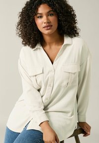 Cream-colored button-up shirt with two chest pockets, long sleeves, and a relaxed fit. Soft texture and subtle ribbed pattern.