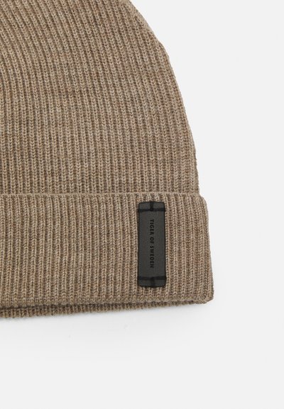 Gorro de malha canelada castanho com uma barra dobrada, apresentando um rótulo retangular preto com texto em relevo. A textura é suave e quente.