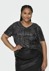 T-shirt nera a maniche corte con paillettes e scollo a V. Indossato su una gonna in pelle nera aderente, che mette in mostra una superficie lucida e strutturata.