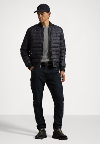 Svart puffjakke med horisontale sømmer, grå genser, mørke cargosbukser og svarte joggesko. Detaljer inkluderer en caps og belte.