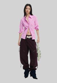 Roosa tikandiga särk, mis on paaritatud tume-lilla lõdva pükstega, millel on tõmbluku detailid. Lisatud lillemustriga vöö ja rohelise kott.