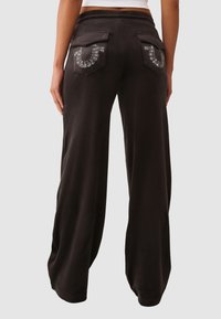 Schwarze, weit geschnittene Hosen aus weichem Stoff, mit zwei Gesäßtaschen, die mit dekorativen silbernen Nähten versehen sind, und einer lockeren Passform.