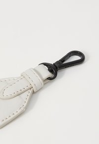 Weißer Leder-Schlüsselanhänger mit genähten Kanten und einem schwarzen Metallclip mit Drehmechanismus. Glatte Textur mit minimalistischem Design.