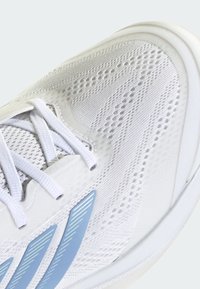 Λευκό αθλητικό παπούτσι με επάνω μέρος από διαπνέον διχτυωτό υλικό με υφασμένα σχέδια, μπλε ρίγες και λευκά κορδόνια. Στρογγυλεμένος σχεδιασμός σόλας.