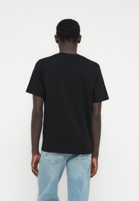 Crna pamučna majica s okruglim izrezom, kratkim rukavima i ravnim rubom, nošena s svijetloplavim trapericama.