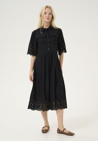 Black shirt dress with short, embroidered sleeves, a button-down front, and a flared hem with scalloped cutouts. Effortless and lightweight.