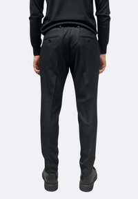 Pantaloni neri sartoriali dal taglio slim, caratterizzati da due tasche posteriori con chiusure a bottone e un tessuto liscio e strutturato.