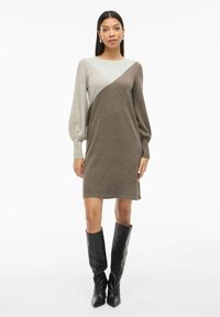 Abito in maglia con design a blocchi di colore in verde chiaro e marrone, con maniche a palloncino e vestibilità dritta, abbinato a stivali neri al ginocchio.