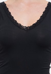 Black top featuring a V-neck with intricate black lace trim along the neckline, made from a smooth, stretchy material.