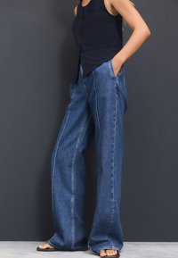 Denimjeans med høj talje og vide ben i mørkeblå med en glat tekstur, udstyret med to sidelommer og kontrasterende sidesømme.