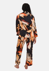 Ensemble de pyjama noir avec un imprimé botanique orange et crème. Le haut a un col et des manches longues ; le pantalon est droit avec une taille élastique.