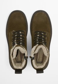 Brązowe zamszowe botki za kostkę z ociepliną z polaru, czarnymi sznurowadłami i wzmocnioną gumową podeszwą. Posiadają wzór w kamuflaż w sznurowaniu.