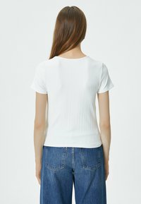 Hvid ribbet kortærmet top med rund halsudskæring, der har en tætsiddende pasform og glat tekstur, parret med denim jeans.