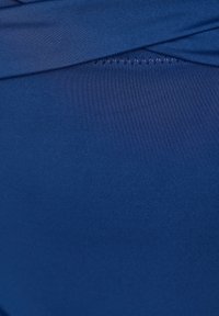 Tmavomodrá plávacia látka s hladkým povrchom a jemným leskom; má prehnutý pás a detail v podobe cik-cak stehu.