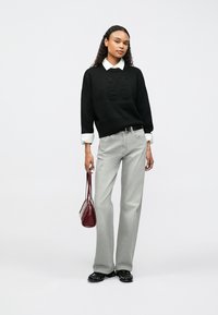 Crni pleteni džemper s utisnutim logotipom "HUGO", bijela košulja s ovratnikom ispod, svijetlosive traperice širokih nogavica i mala bordo torbica.