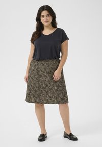 T-shirt noir à col en V associé à une jupe imprimée léopard jusqu'aux genoux. La jupe a une taille élastique ; le mannequin porte des mocassins noirs.