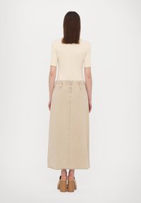 Beige denim-maksihame, jossa on rispaantunut helma, korkea vyötärö, kaksi takataskua ja vyölenkit, yhdistettynä vaaleanruskeisiin korkokenkiin.