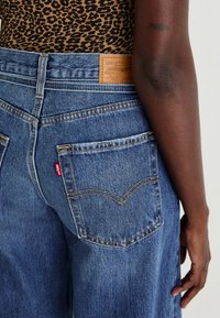 Vaaleansiniset Levi's farkut, joissa on tekstuuripinta. Farkuissa on kaksi takataskua, joissa on punainen logo-etiketti ja ruskea nahkabrändäys vyötäröllä.